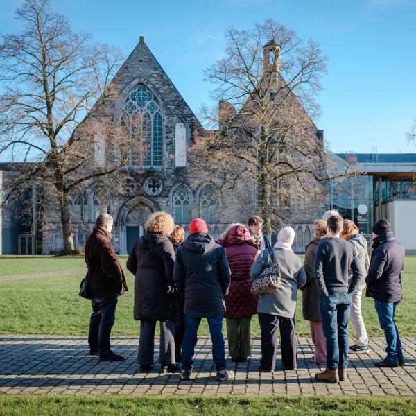 Afbeelding van een groep mensen die voor het gebouw van De Bijloke aandachtig luisteren naar een gids. 