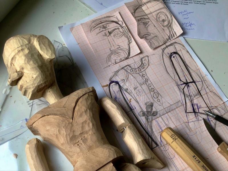 Een houten pop met ontwerpschetsen in potlood en een mesje ernaast