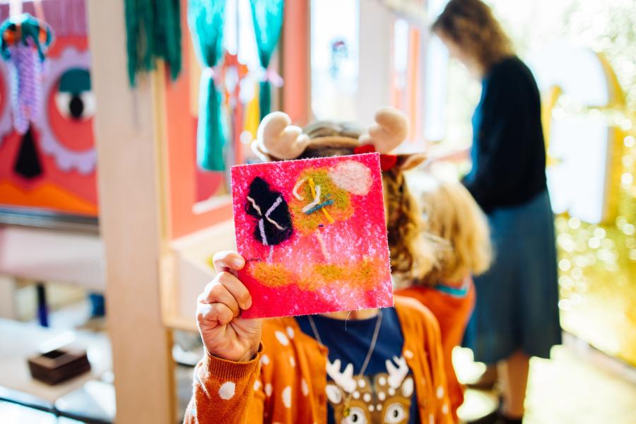 Een kind toont haar zelfgemaakte textielcollage.